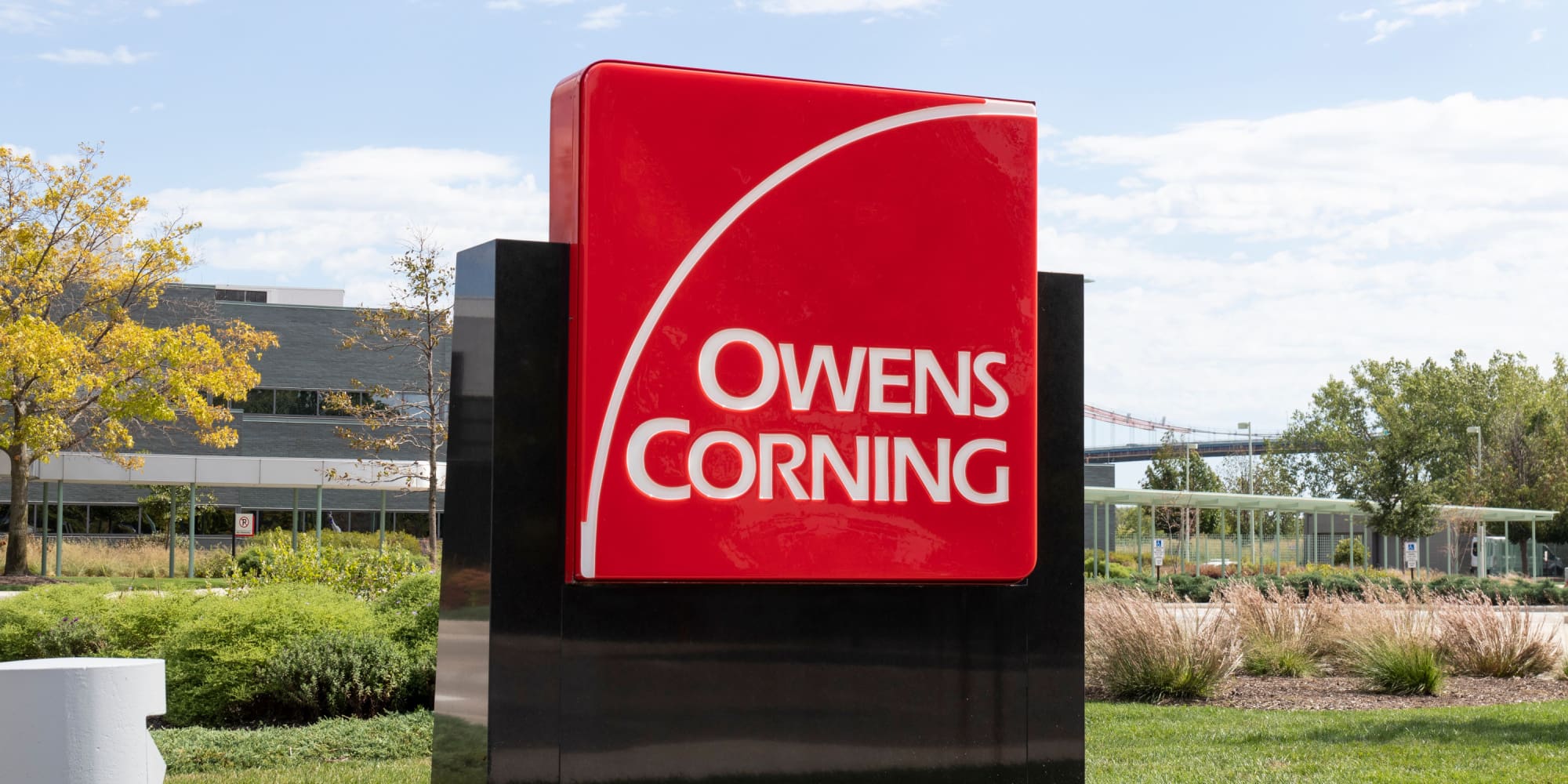 A bright red "Owens Corning" sign stands outside on a sunny day.