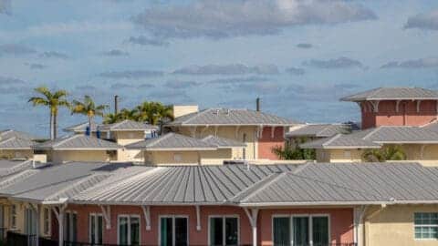 An apartment is shown with a pristine new metal roof in Florida with palm trees along the building.