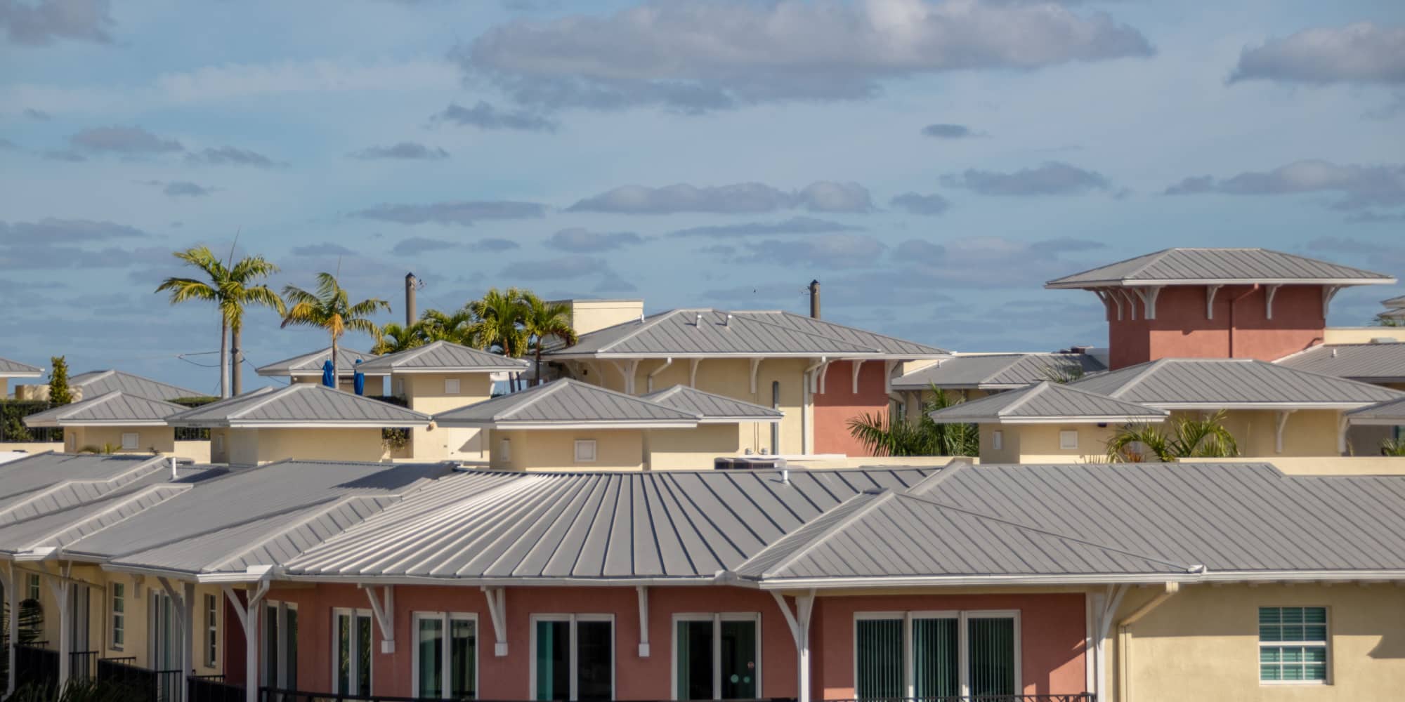An apartment is shown with a pristine new metal roof in Florida with palm trees along the building.