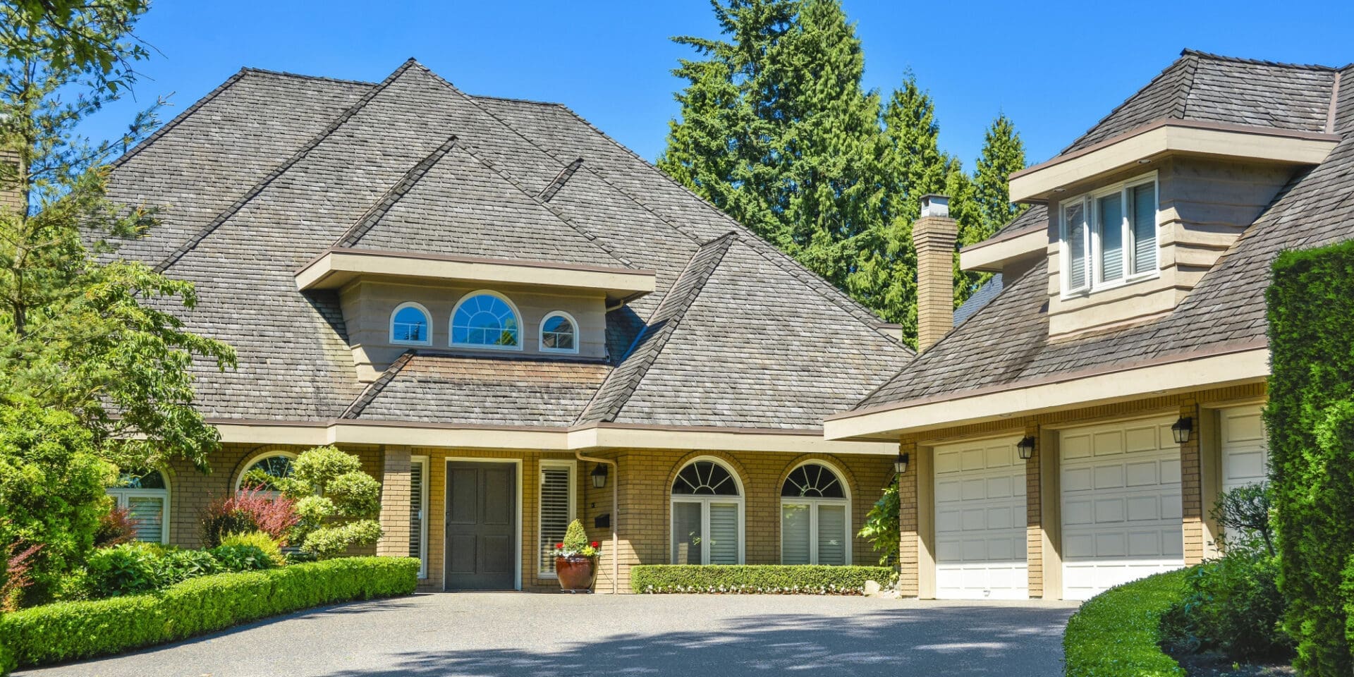 A beautiful, multi-story house is seen with a tan architectural shingle roof.