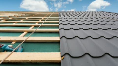 A roof in the middle of replacement shows the right half covered in metal sheets and the left half with wood decking exposed.