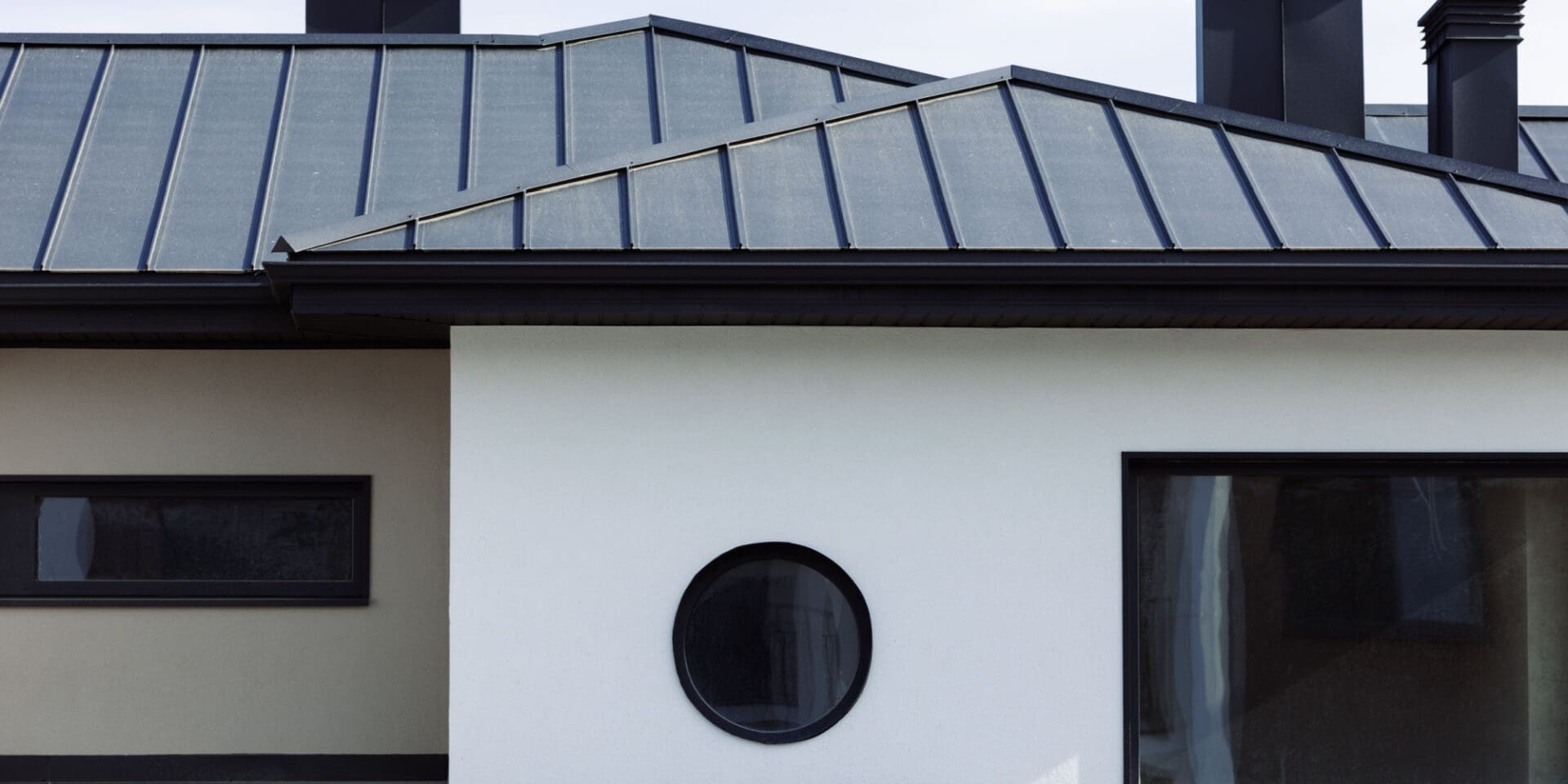 A beautiful, white modern home is shown with a new black standing seam roof.