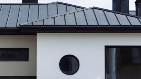 A beautiful, white modern home is shown with a new black standing seam roof.