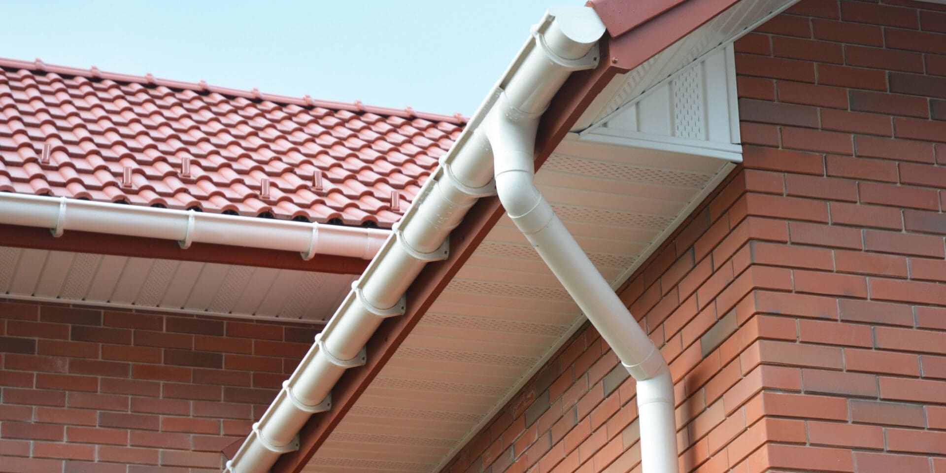 A beautiful soffit and fascia are shown on the side of a residential sloped roof with red tile.